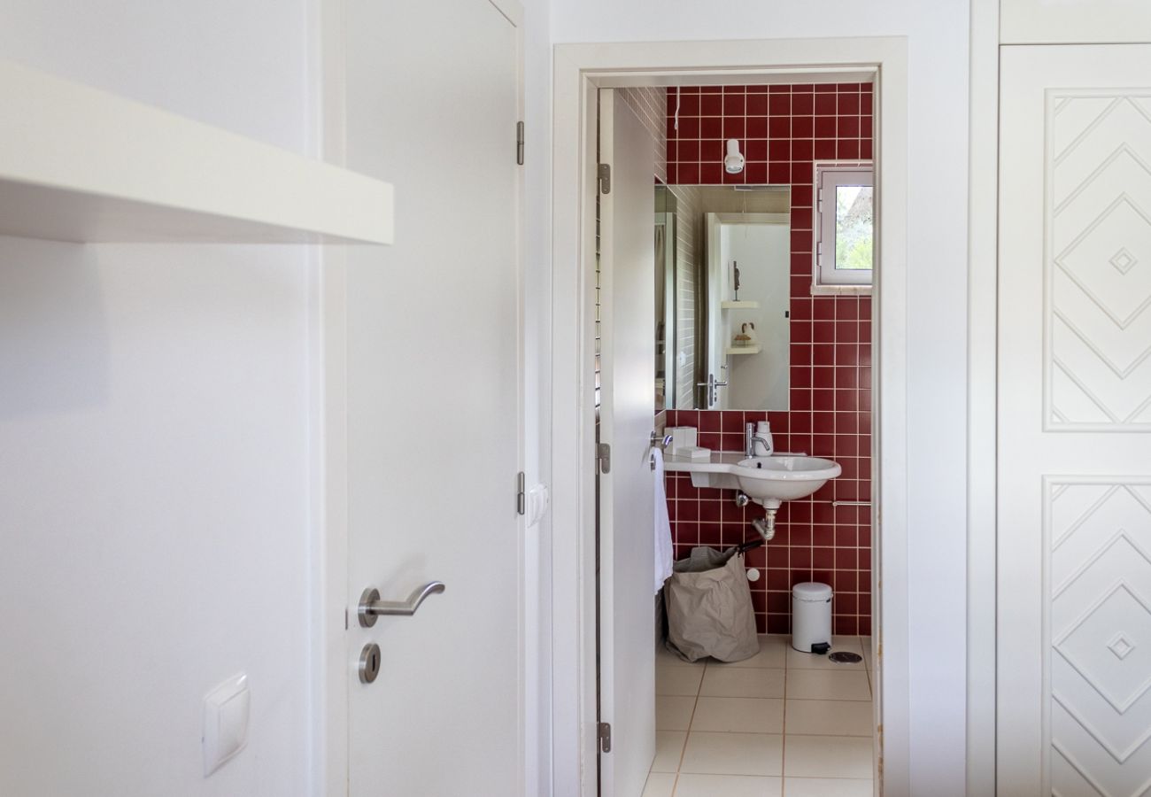 Modern bathroom with red tiles, a large mirror, and a white sink, seen through the door.