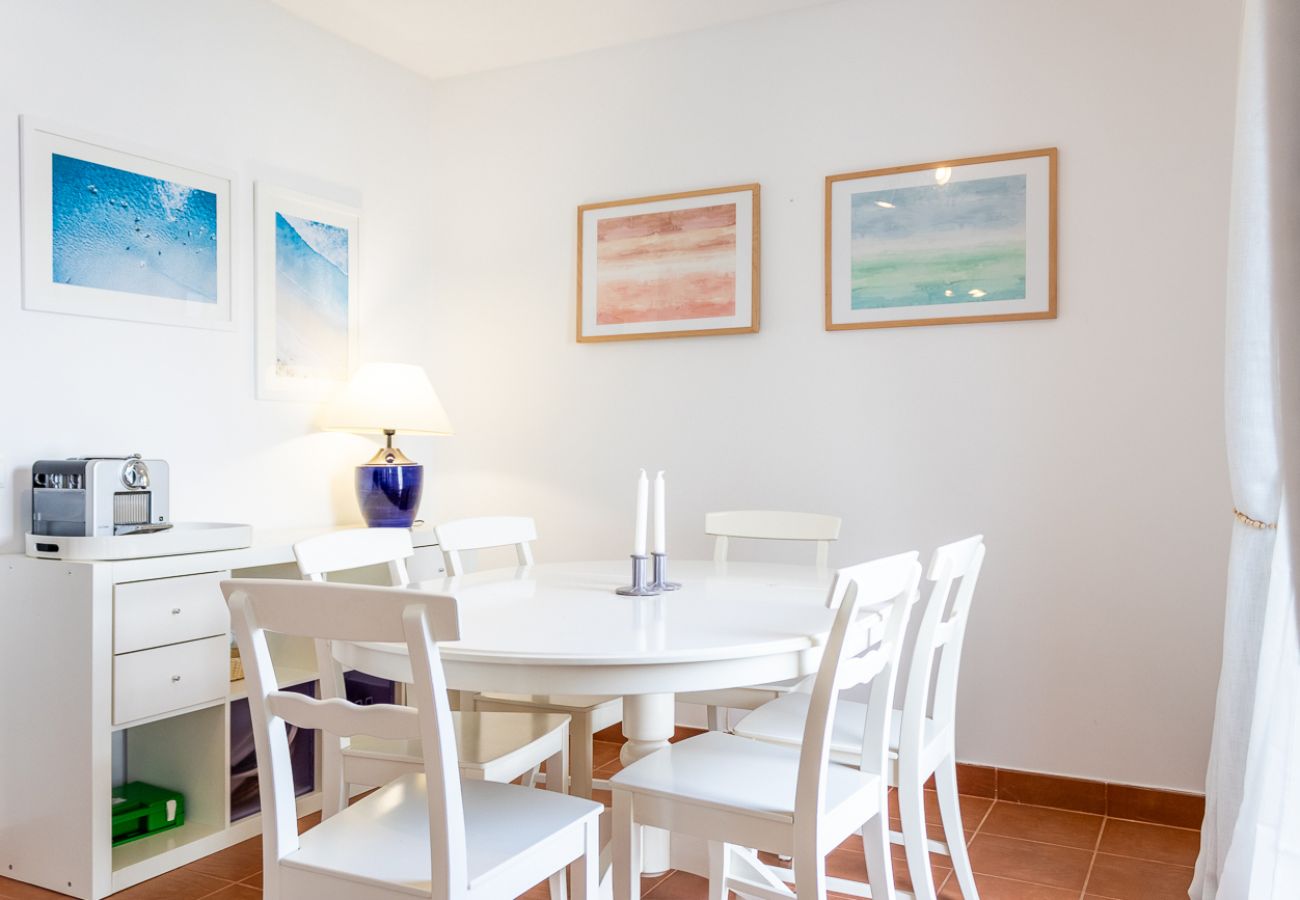 Dining room with a white round table, four chairs, a table lamp, and decorative paintings on the wall.