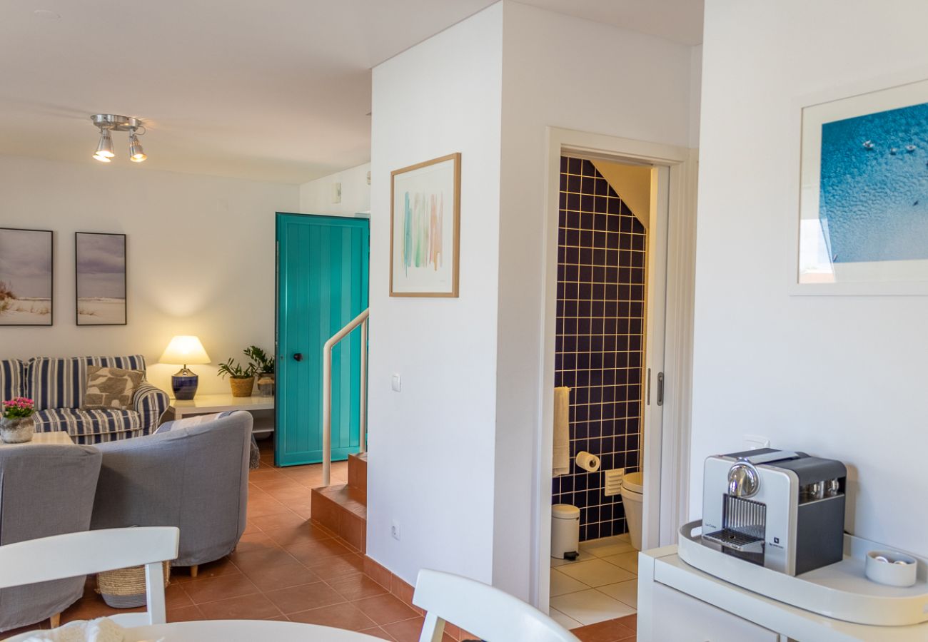 Living room with blue sofa, entrance hallway with turquoise door, and a bathroom in the background.
