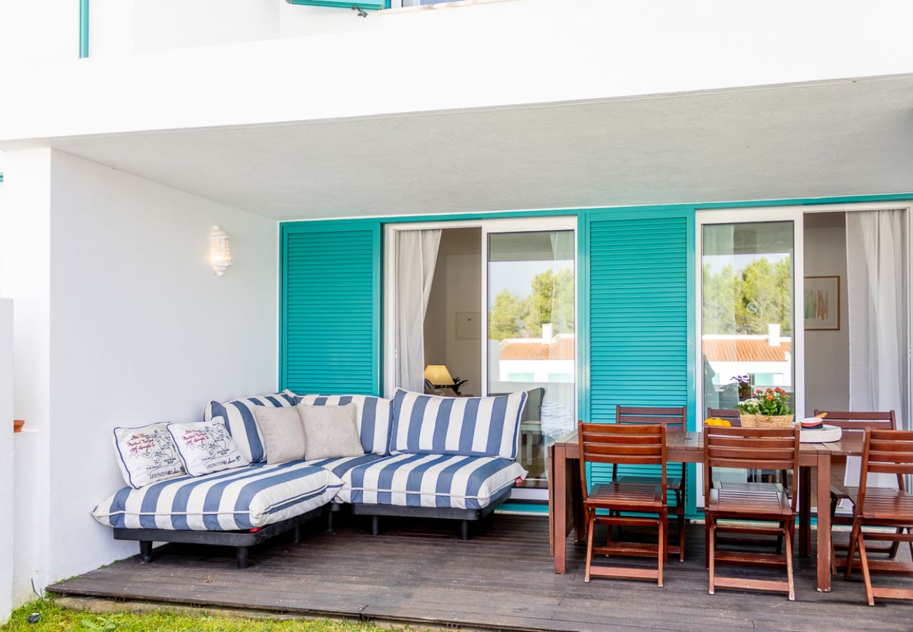 Covered terrace with a blue and white striped sofa, wooden dining table, and sliding doors overlooking the garden.