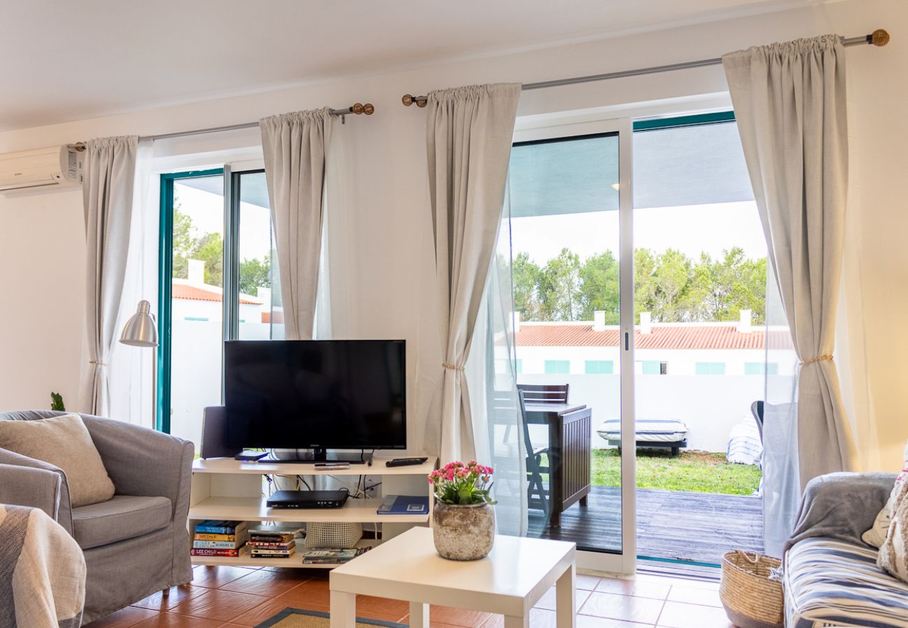 Living room with a sofa, armchair, coffee table, television, and a balcony overlooking the outdoor area.