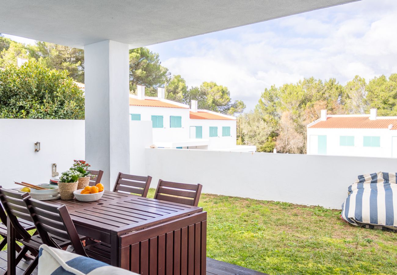 Covered terrace with a wooden dining table, chairs, and a view of a green garden.