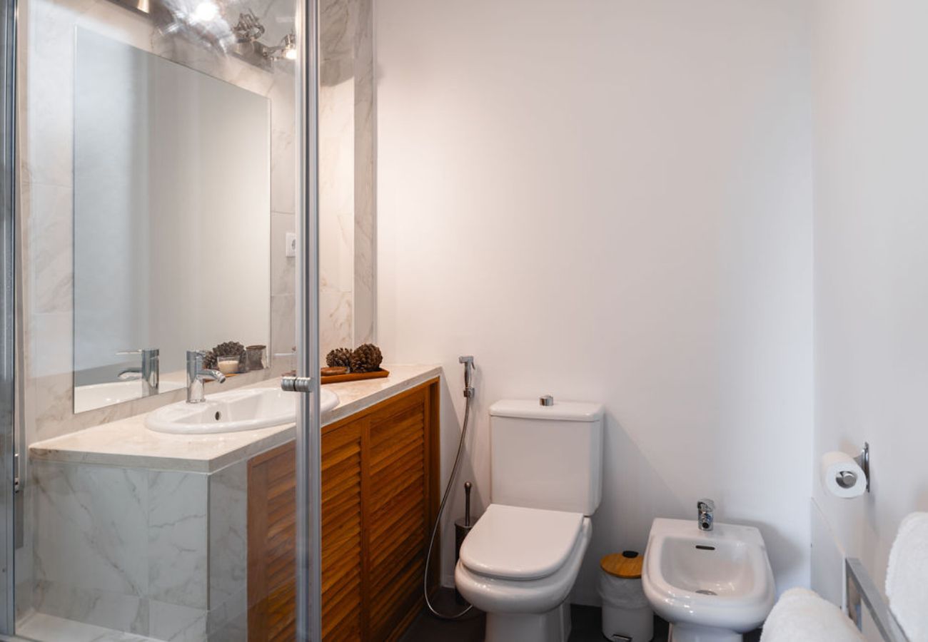 Elegant bathroom featuring a glass-enclosed shower, marble countertop with wooden vanity, toilet, and bidet.