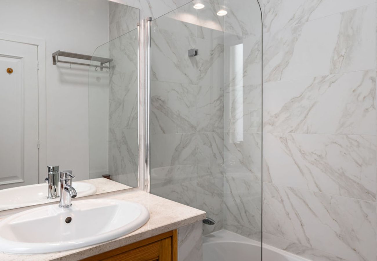 Modern bathroom with marble walls, double sink, and shower with transparent glass enclosure.