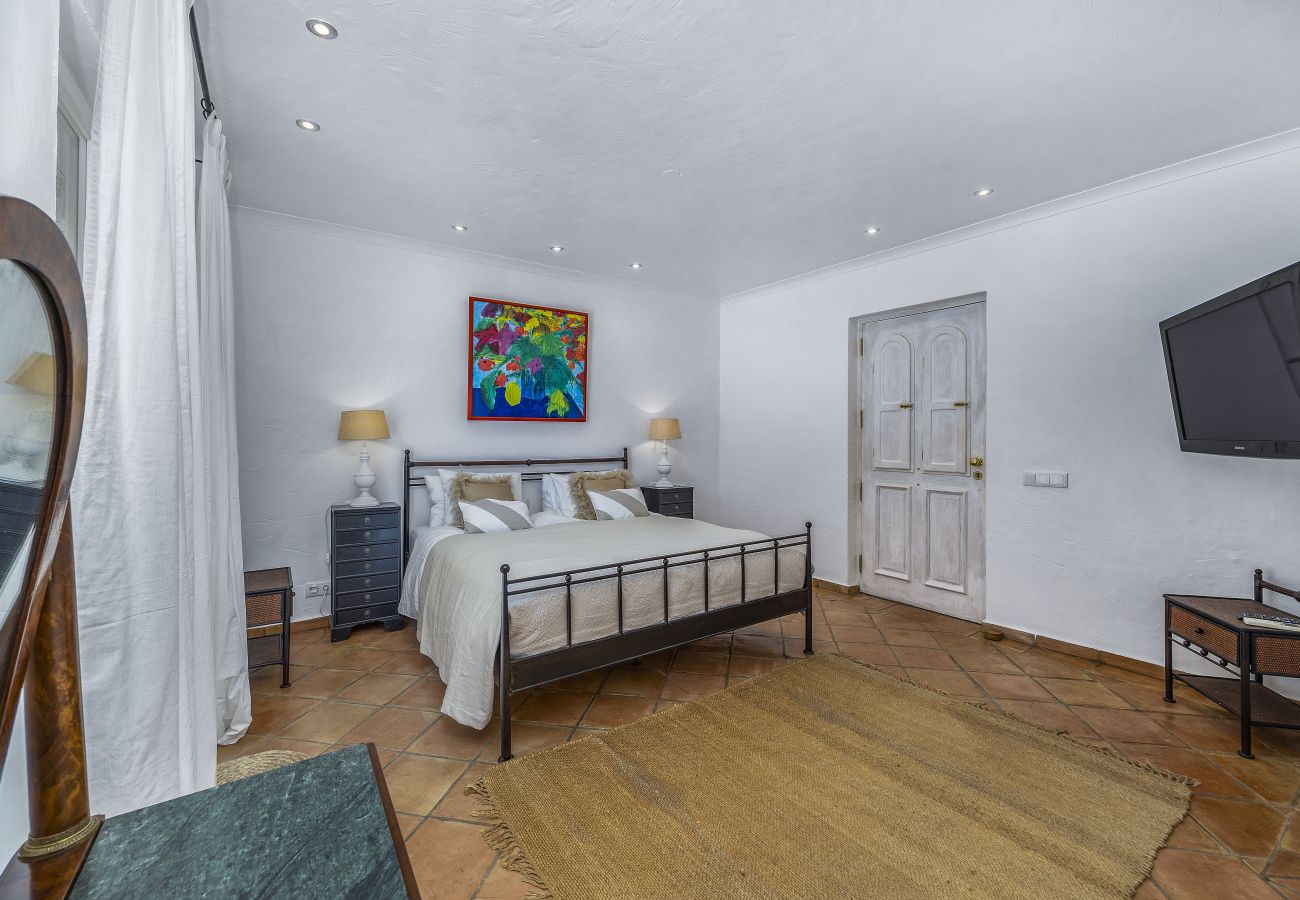 Elegant bedroom with an iron bed, large rug, wall-mounted TV, and contemporary decor featuring colorful artwork.
