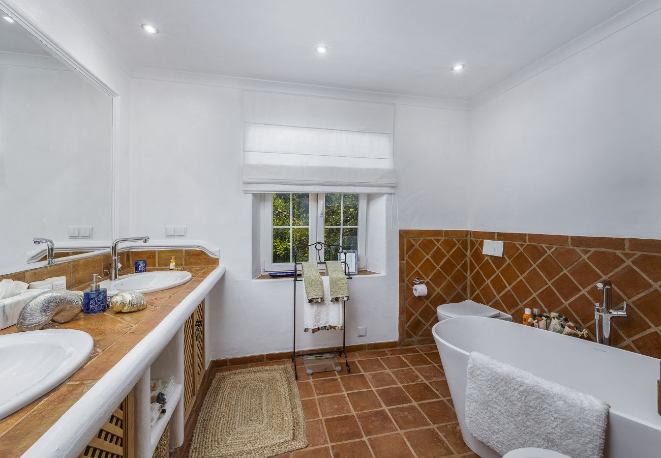 Spacious bathroom featuring a double sink, freestanding bathtub, and rustic wood and tile details. Bright atmosphere with natural decorative elements.
