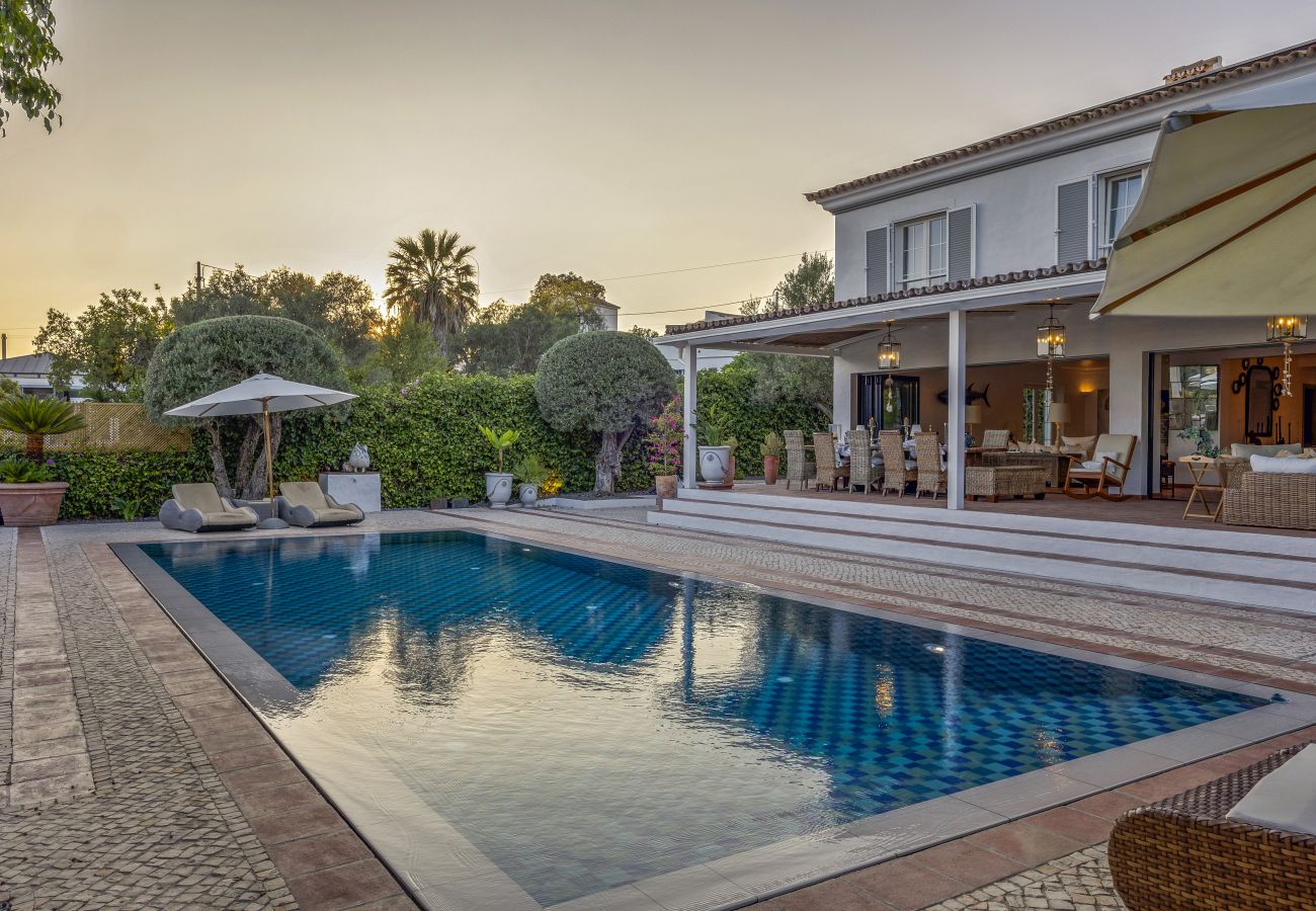 Blue pool reflecting the sunset, surrounded by comfortable sun loungers and a sophisticated ambiance with cozy lighting.