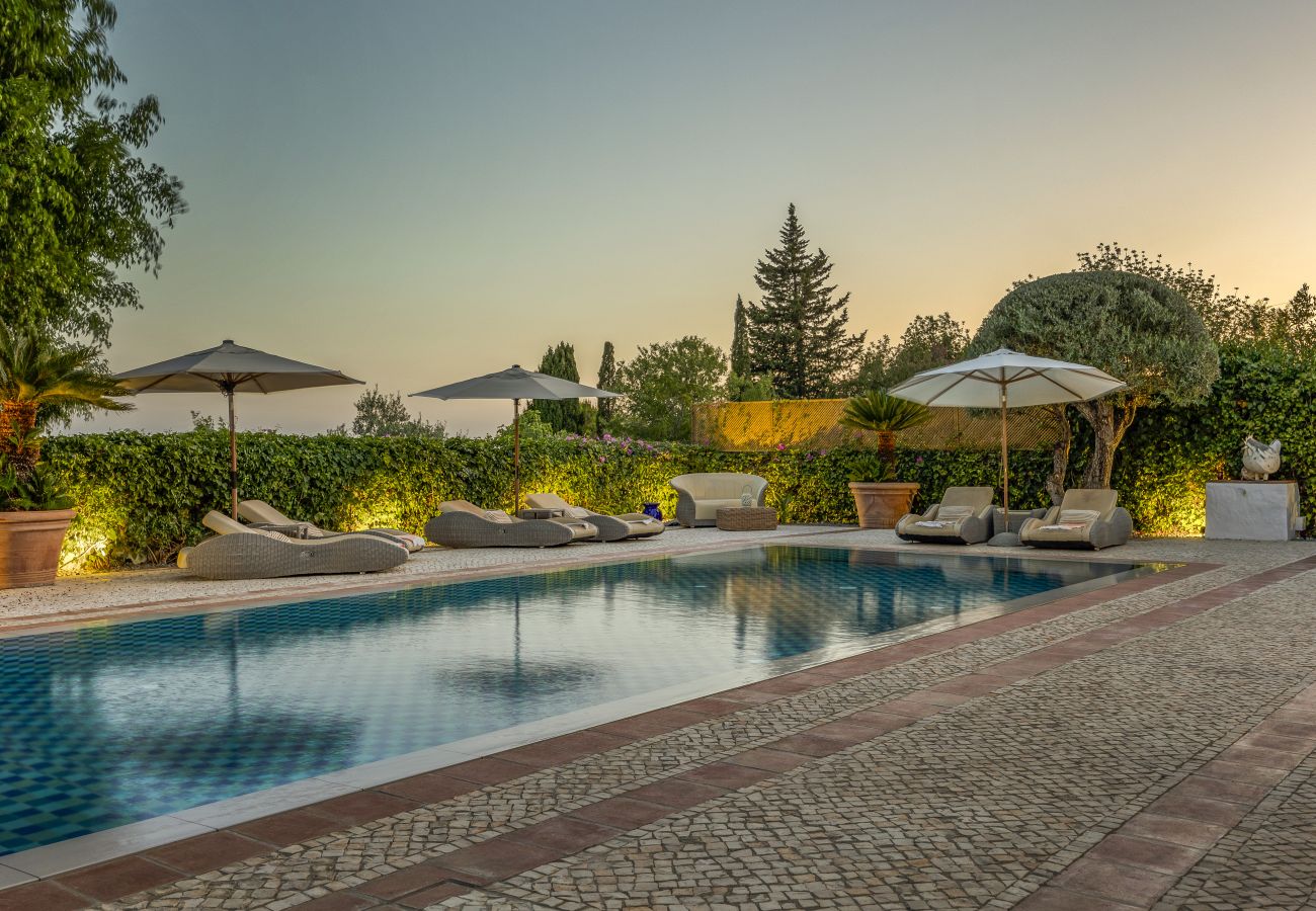 Sophisticated outdoor area featuring a blue-tiled pool, comfortable sun loungers, and elegant umbrellas at sunset.