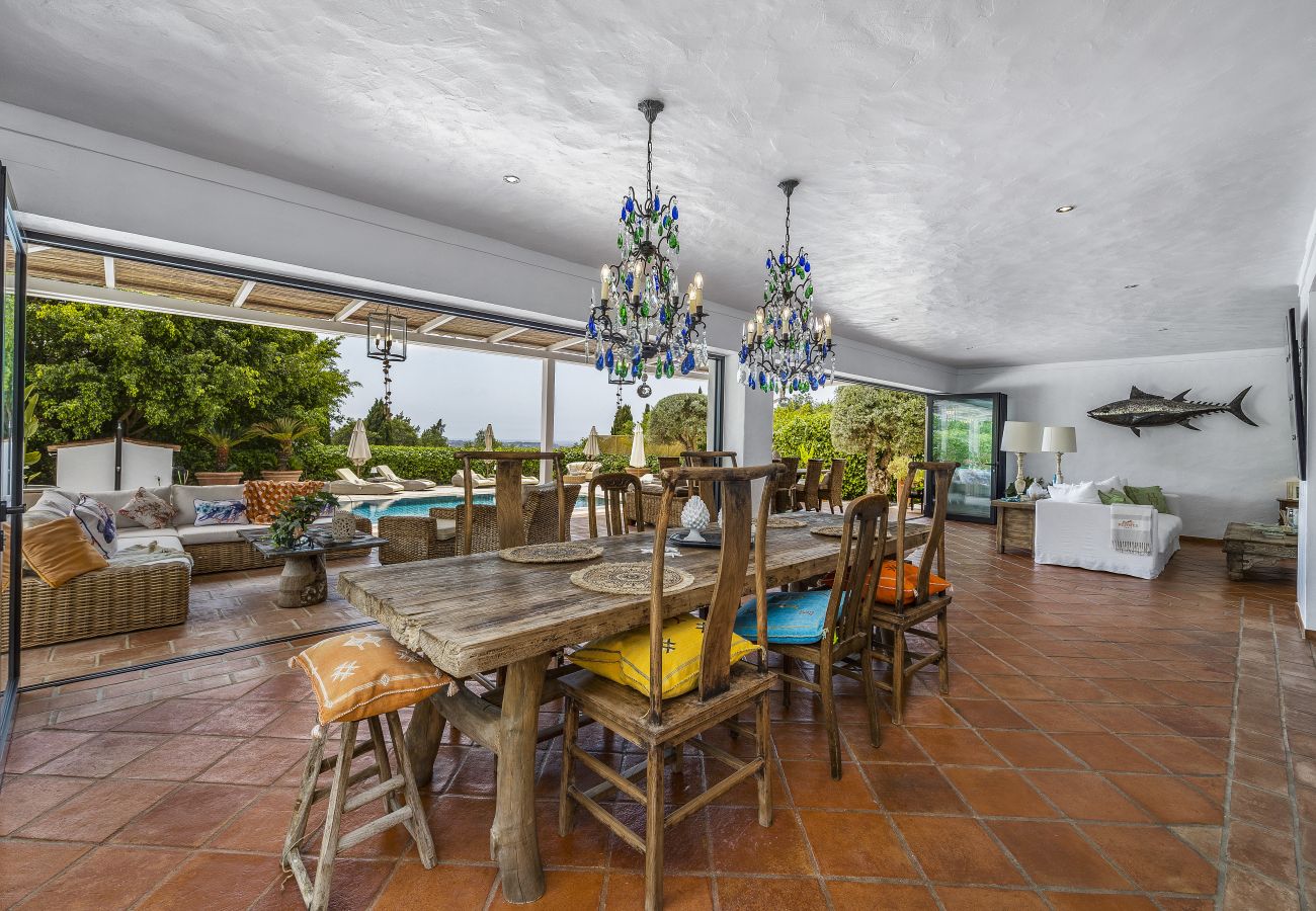 Spacious dining room with a rustic wooden table, elegant chairs, and blue crystal chandeliers, seamlessly connected to the outdoor area.