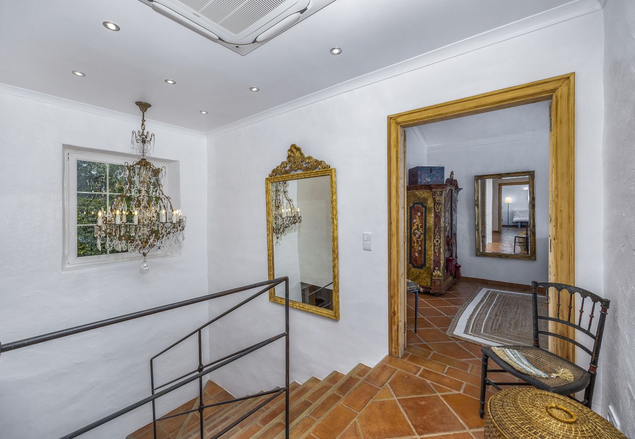 Elegant upper hall with modern railing, classic chandelier, golden mirror, and entrance to a bedroom decorated with vintage furniture.