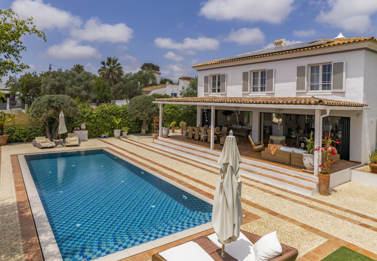  Aerial image of a sophisticated house with a bright blue swimming pool, surrounded by a green garden and an elegant leisure space.