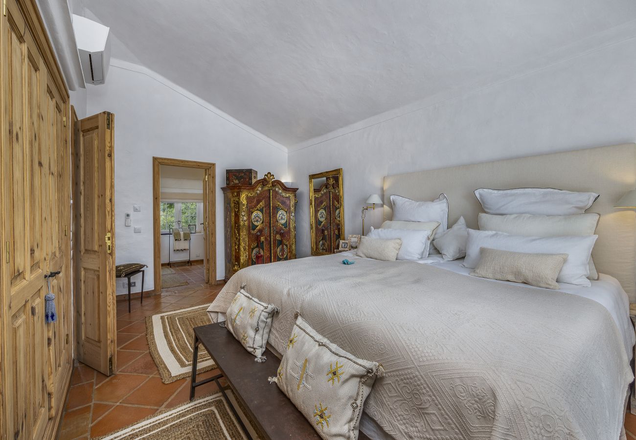 Spacious master bedroom featuring a comfortable bed, upholstered headboard, vintage furniture, and wooden wardrobes. Soft lighting and decorative deta