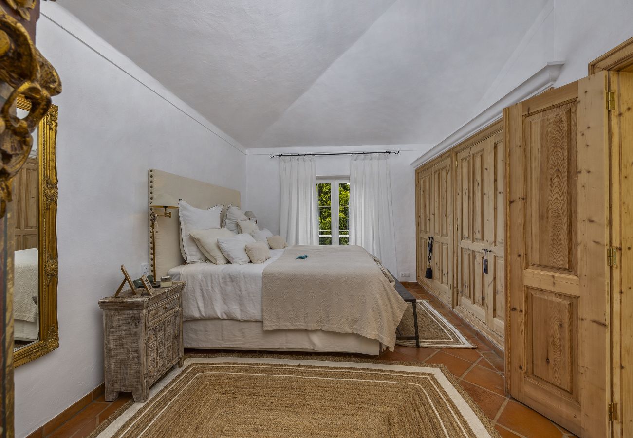 Spacious master bedroom featuring a comfortable bed, upholstered headboard, vintage furniture, and wooden wardrobes. Soft lighting and decorative deta