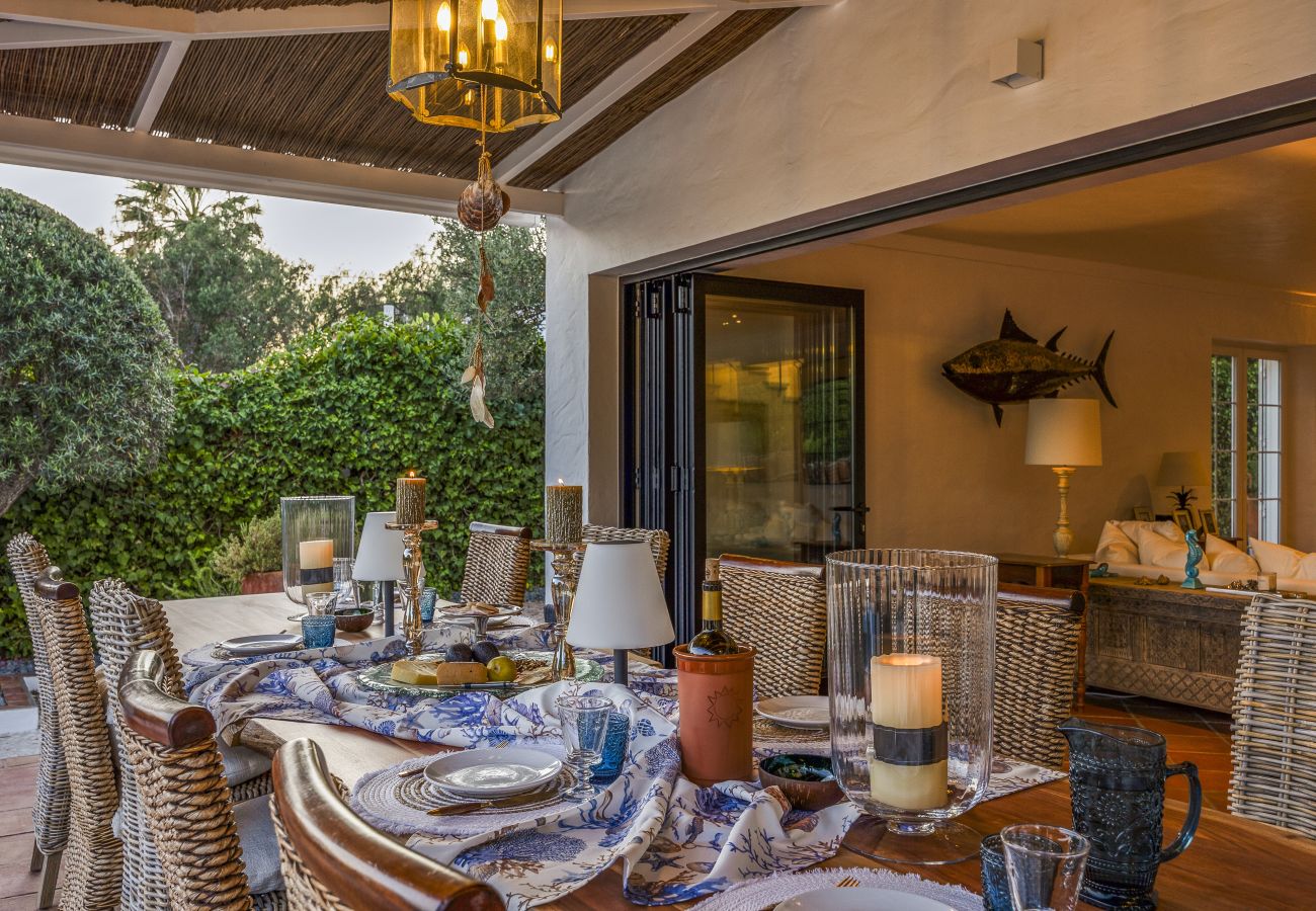 Elegantly set outdoor dining table with lit candles and a view of a lush garden at sunset.