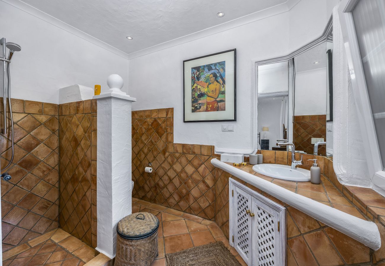 Elegant bathroom featuring a double sink, large mirrors, open shower with earth-toned tiles, and charming decor.