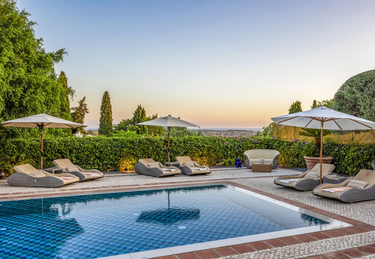 Shimmering blue pool surrounded by comfortable sun loungers and elegant umbrellas, with a stunning sunset in the background.