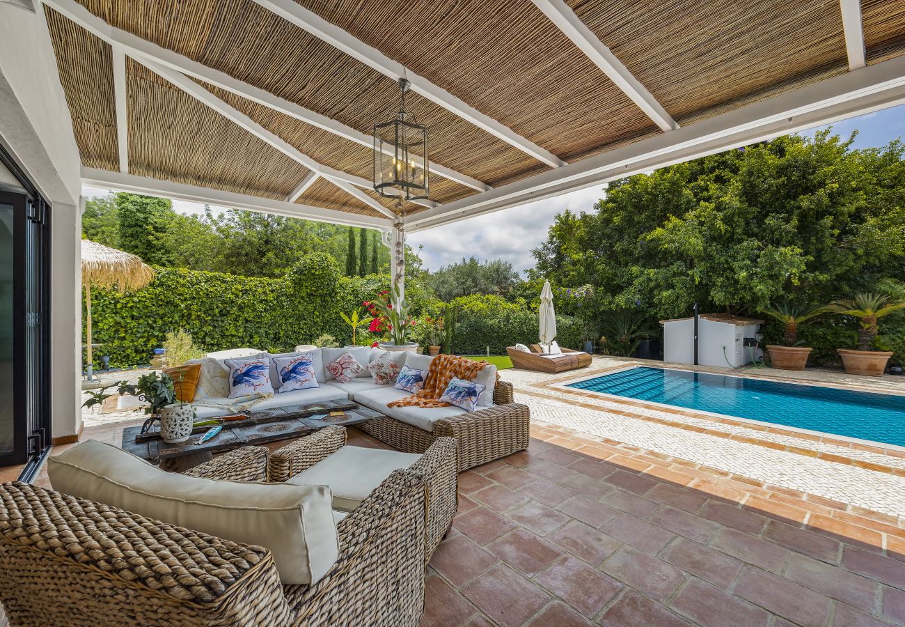 Cozy outdoor space with comfortable wicker furniture, covered by a straw roof, overlooking the pool and a lush garden.