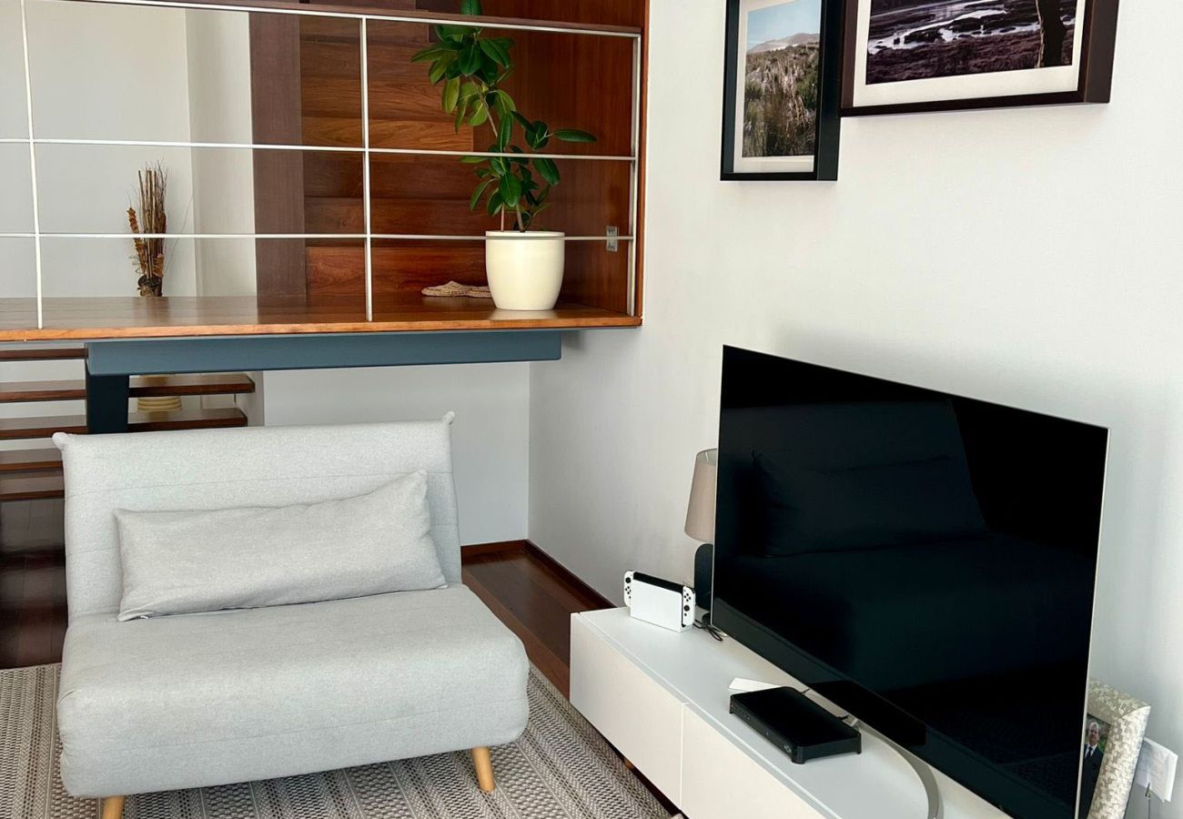 Living room with a cozy sofa, TV, and modern decor, featuring a decorative railing on the upper floor.