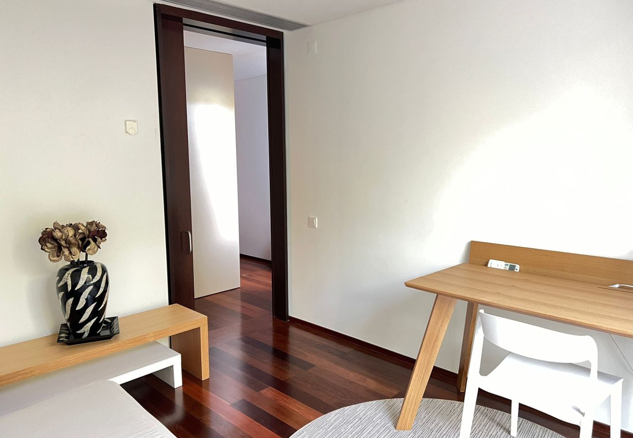 Bright bedroom with a wooden desk, white chair, and wooden floor, overlooking the hallway.