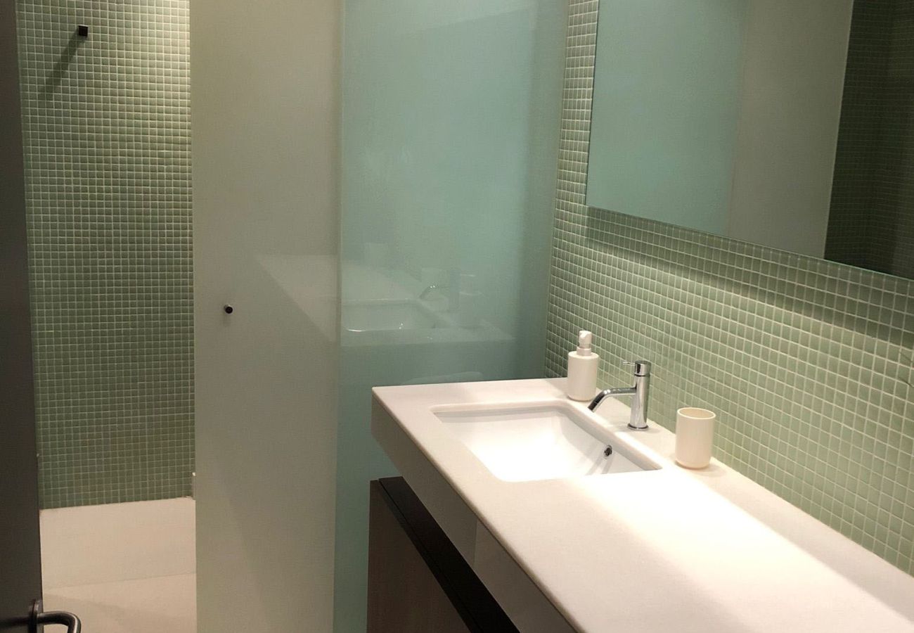 Elegant bathroom with green mosaic-tiled walls, double sink, and glass-enclosed shower.