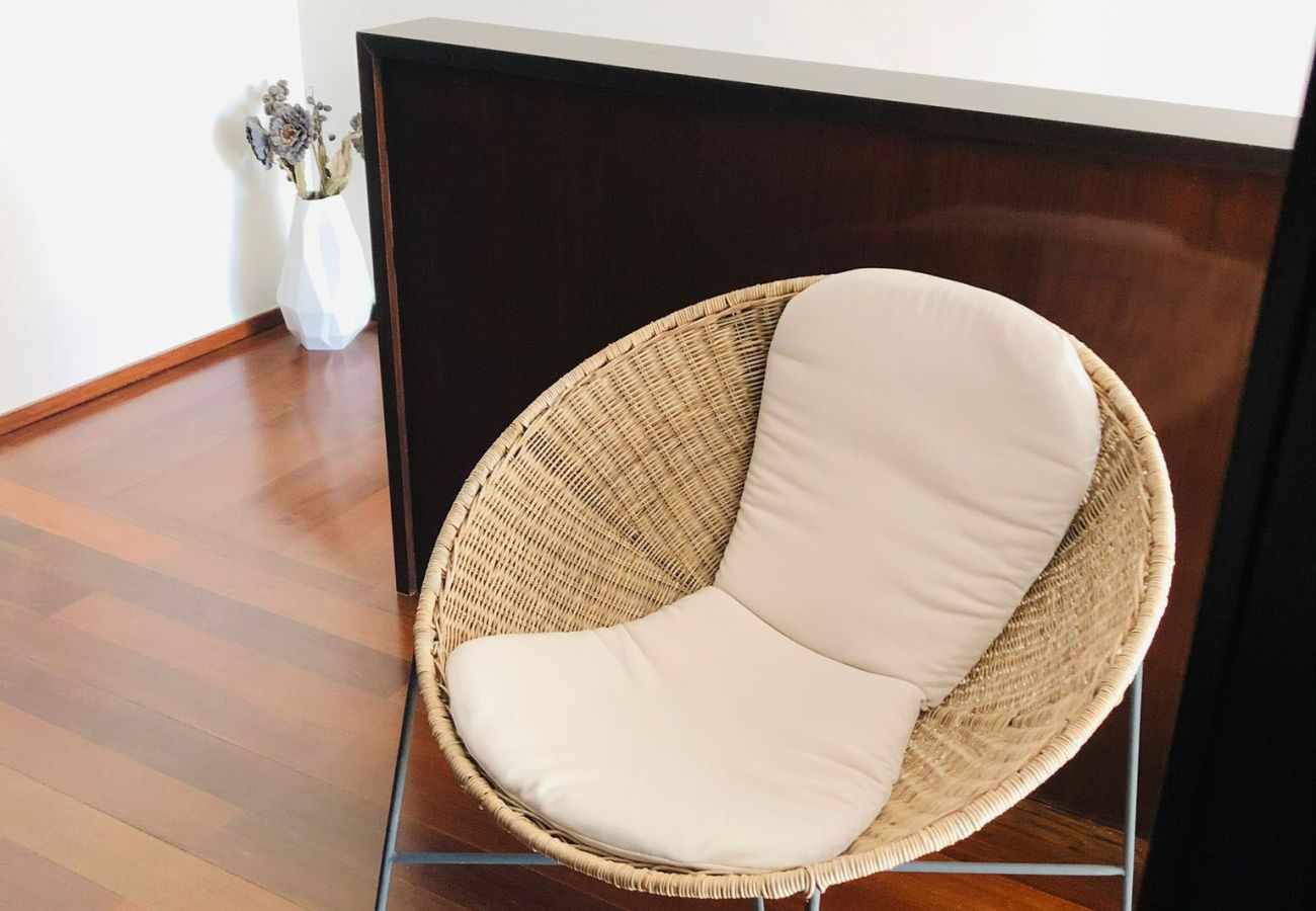 Wicker chair with a white cushion, placed in a sophisticated space with wooden flooring and minimalist decor.