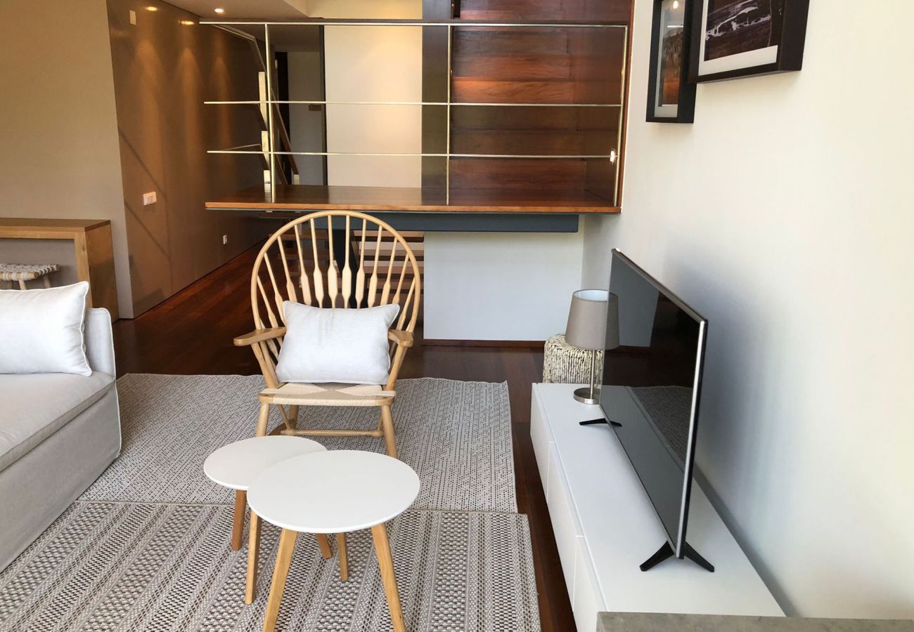 Elegant living room with a cozy sofa, designer chair, coffee table, and TV. The space features a stylish rug, built-in lighting, and a mezzanine in th