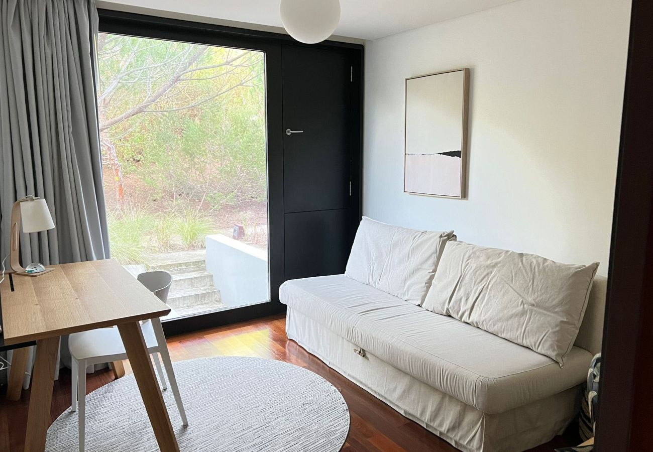 Bedroom with a comfortable sofa bed, wooden desk, and a large window overlooking the garden.