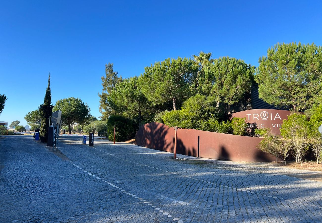 View of the condominium entrance in Troia, featuring well-maintained gardens and a peaceful street in the background.