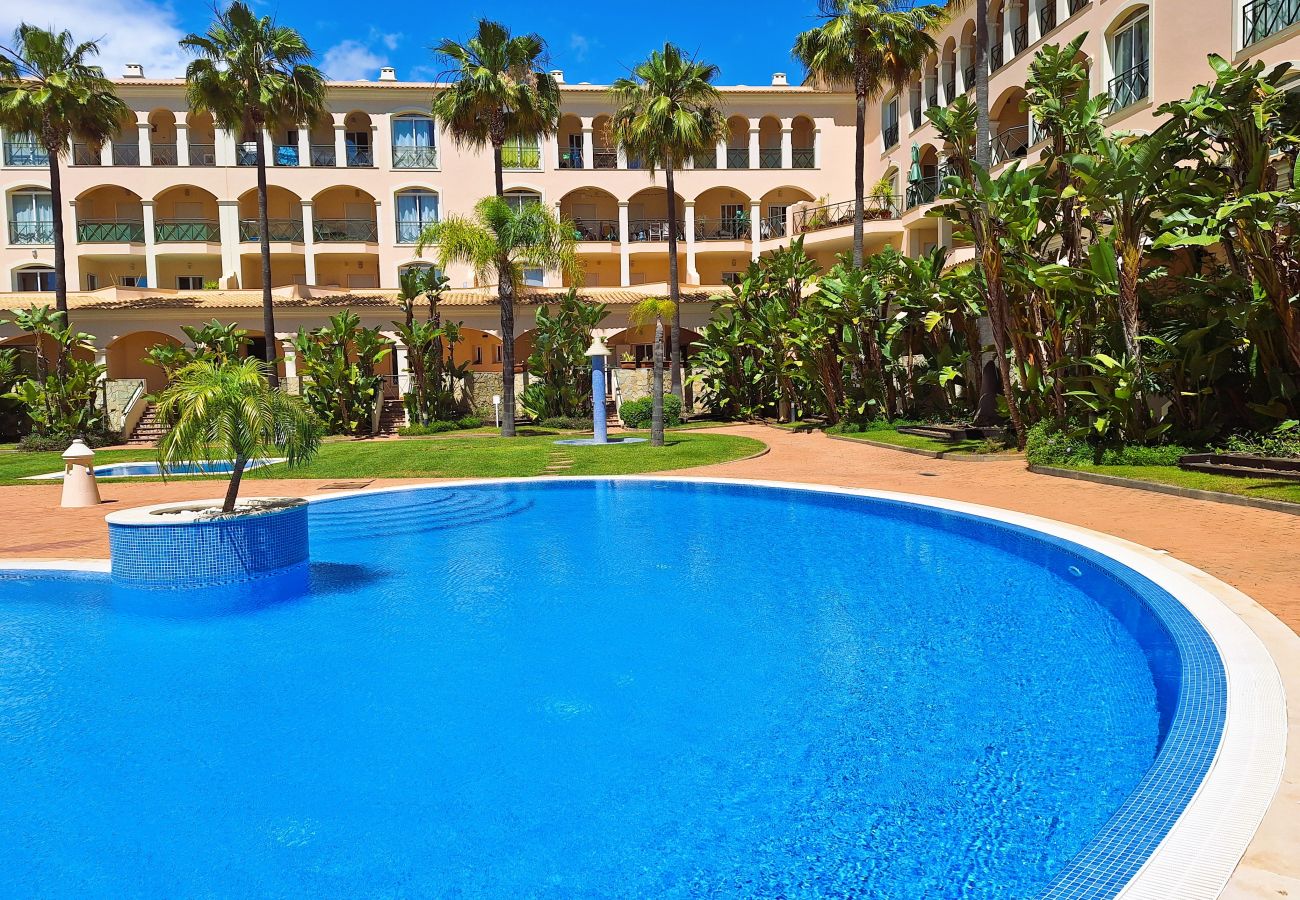 Spacious pool with crystal-clear blue water, surrounded by lush gardens and a sophisticated building in the background.