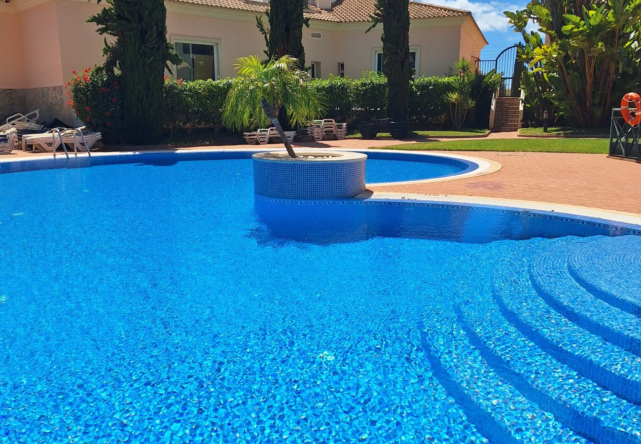 View of a crystal-clear blue pool with access stairs, surrounded by a well-maintained garden and lush greenery.