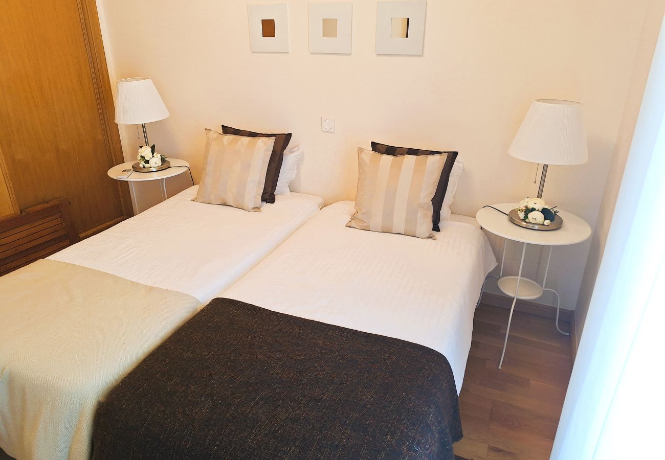 View of a cozy bedroom with two single beds, elegant bedding, and sheer curtains allowing natural light.