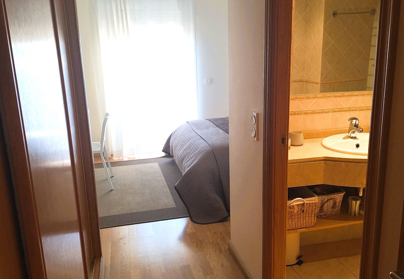 View of the hallway leading to the master bedroom and private bathroom, featuring wooden flooring and natural lighting.