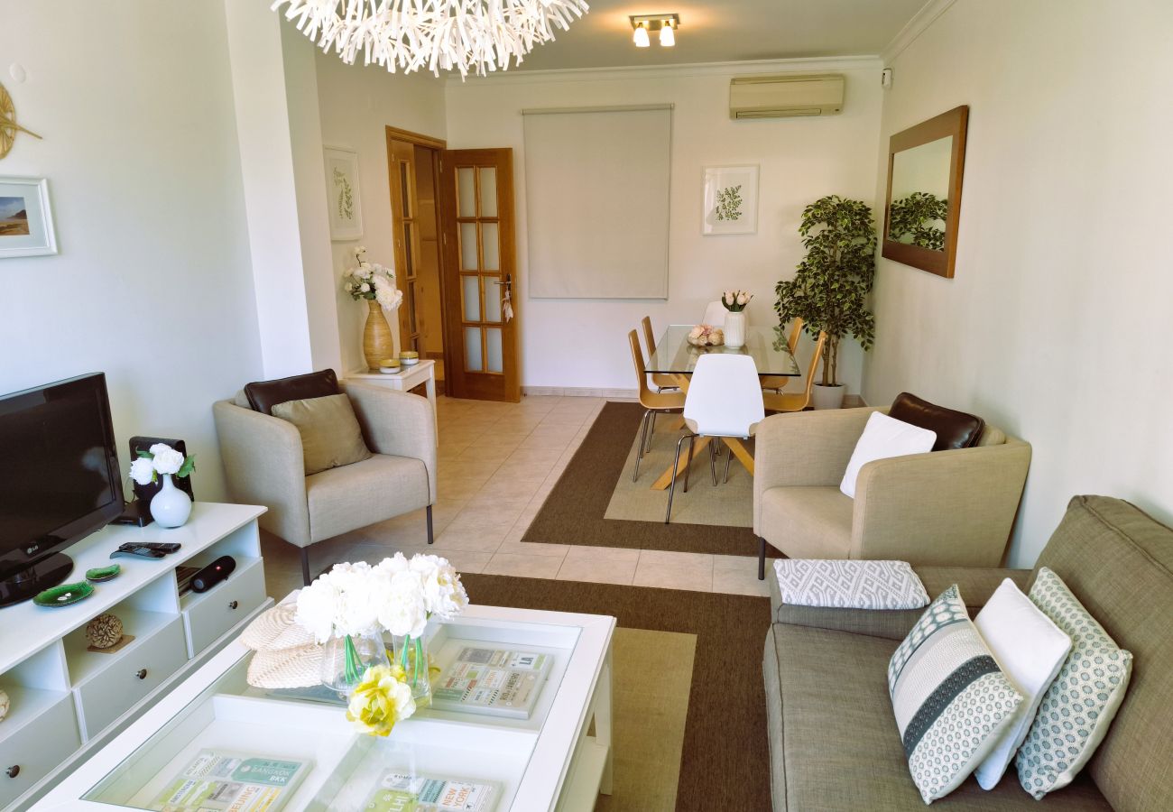 Sophisticated living room with a comfortable sofa, decorated coffee table, and dining area in the background, in a well-lit space.