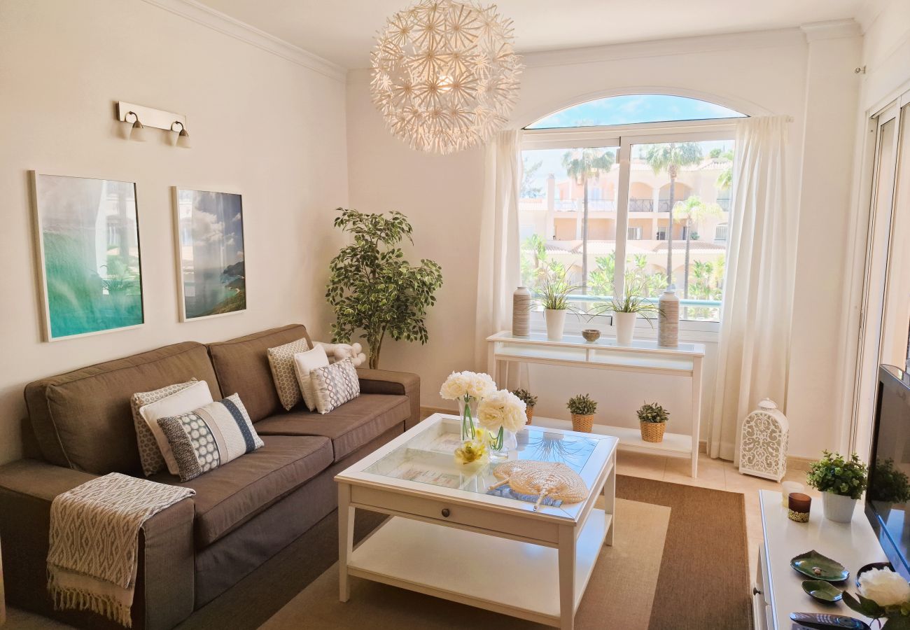 Living room decorated in neutral tones, featuring a comfortable sofa, coffee table, and large windows overlooking the garden.