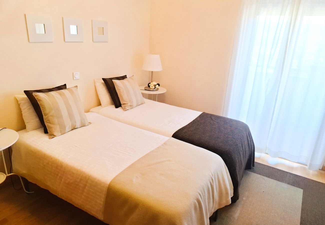 View of a cozy bedroom with two single beds, elegant bedding, and sheer curtains allowing natural light.