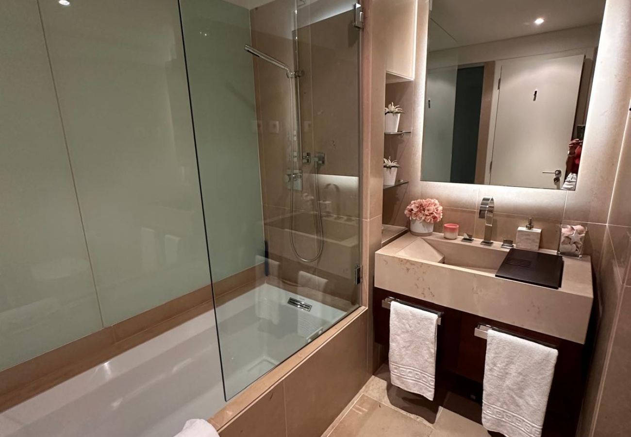 Elegant and sophisticated bathroom with indirect lighting. Features a spacious bathtub with a glass partition, a large mirror with built-in lighting, 