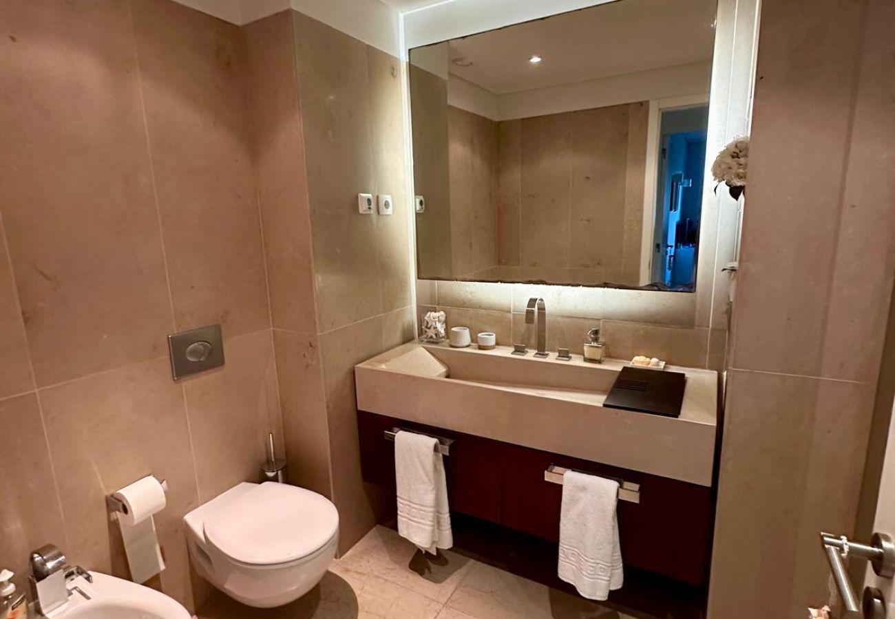  Spacious bathroom with neutral-toned finishes. Features a double sink, suspended toilet, bidet, and a large illuminated mirror, creating a sophistica