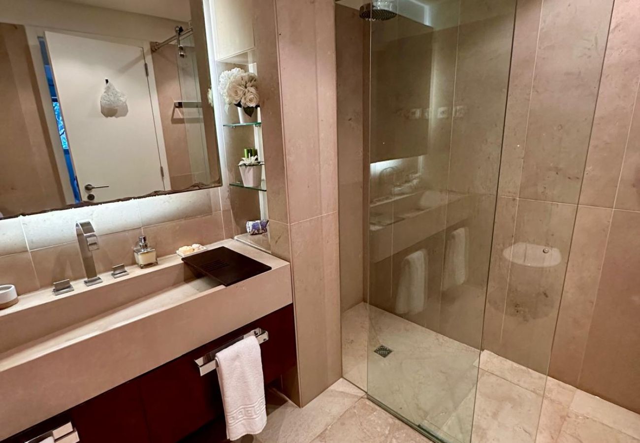 Spacious bathroom with neutral-toned finishes. Features a double sink, suspended toilet, bidet, and a large illuminated mirror, creating a sophisticat