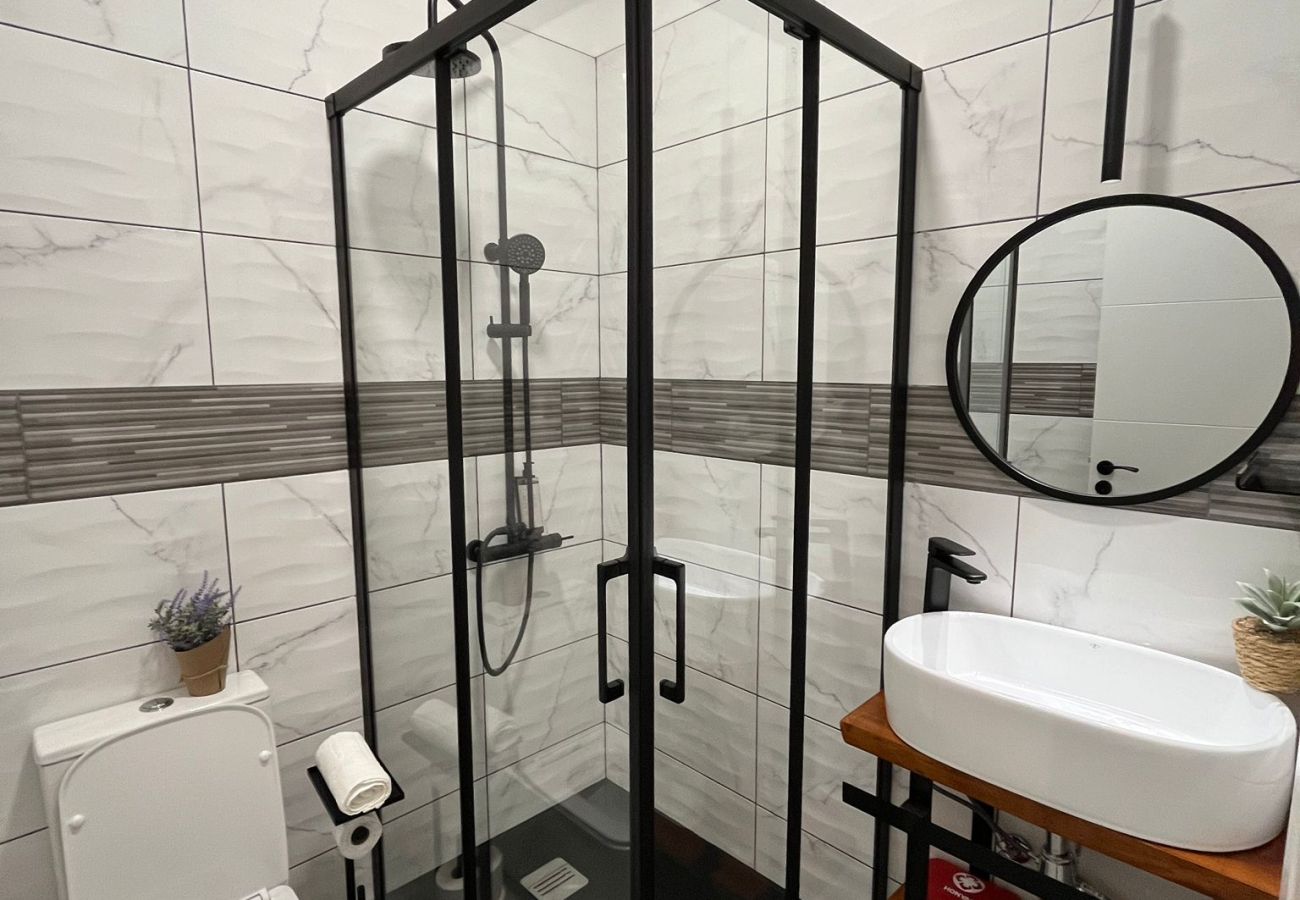 Bathroom with black glass shower enclosure, modern shower, white designer sink, and round mirror.