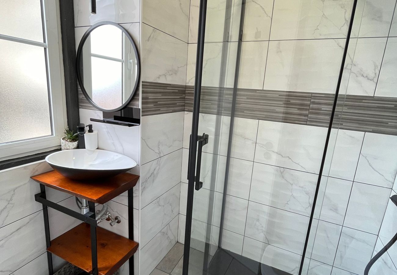 Bathroom with glass-enclosed shower, round sink with mirror, and minimalist decor in light tones.