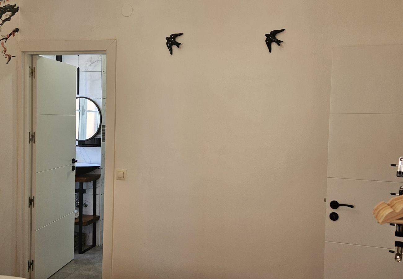 Bedroom with double bed, wall decor with swallows, open clothes rack, and door to the bathroom.