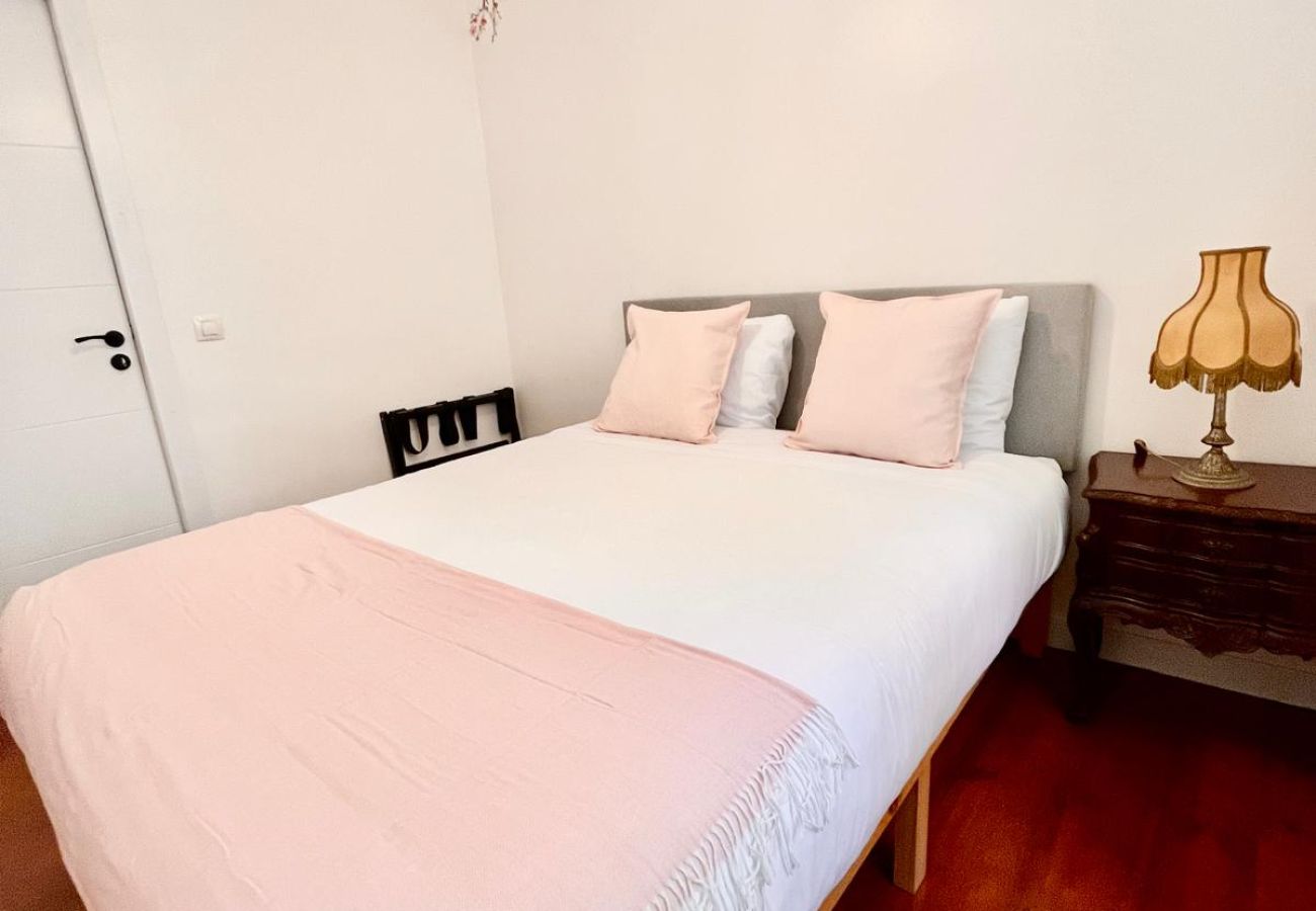 Bedroom with a double bed, white bedding with a pink throw, elegant pillows, and a classic lamp.