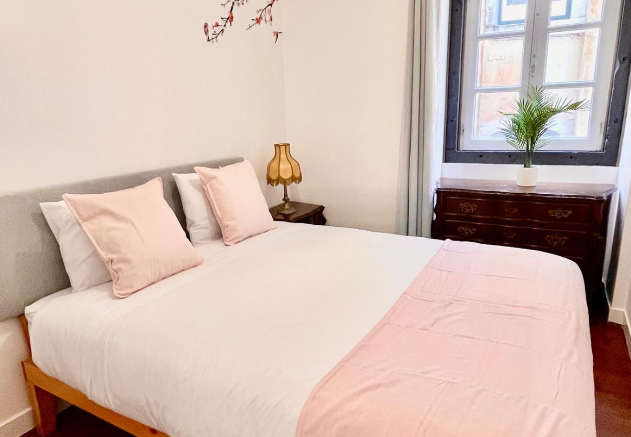 Bright room with a double bed, pink bedding, decorative pillows, and a large window.