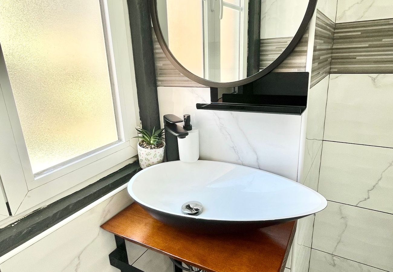 Bathroom with glass-enclosed shower, round sink with mirror, and minimalist decor in light tones.