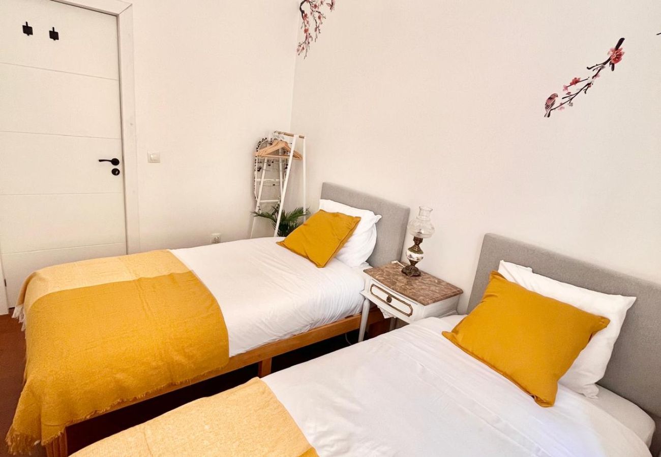 Bedroom with two single beds, white bedding with yellow accents, classic lighting, and sophisticated decoration.