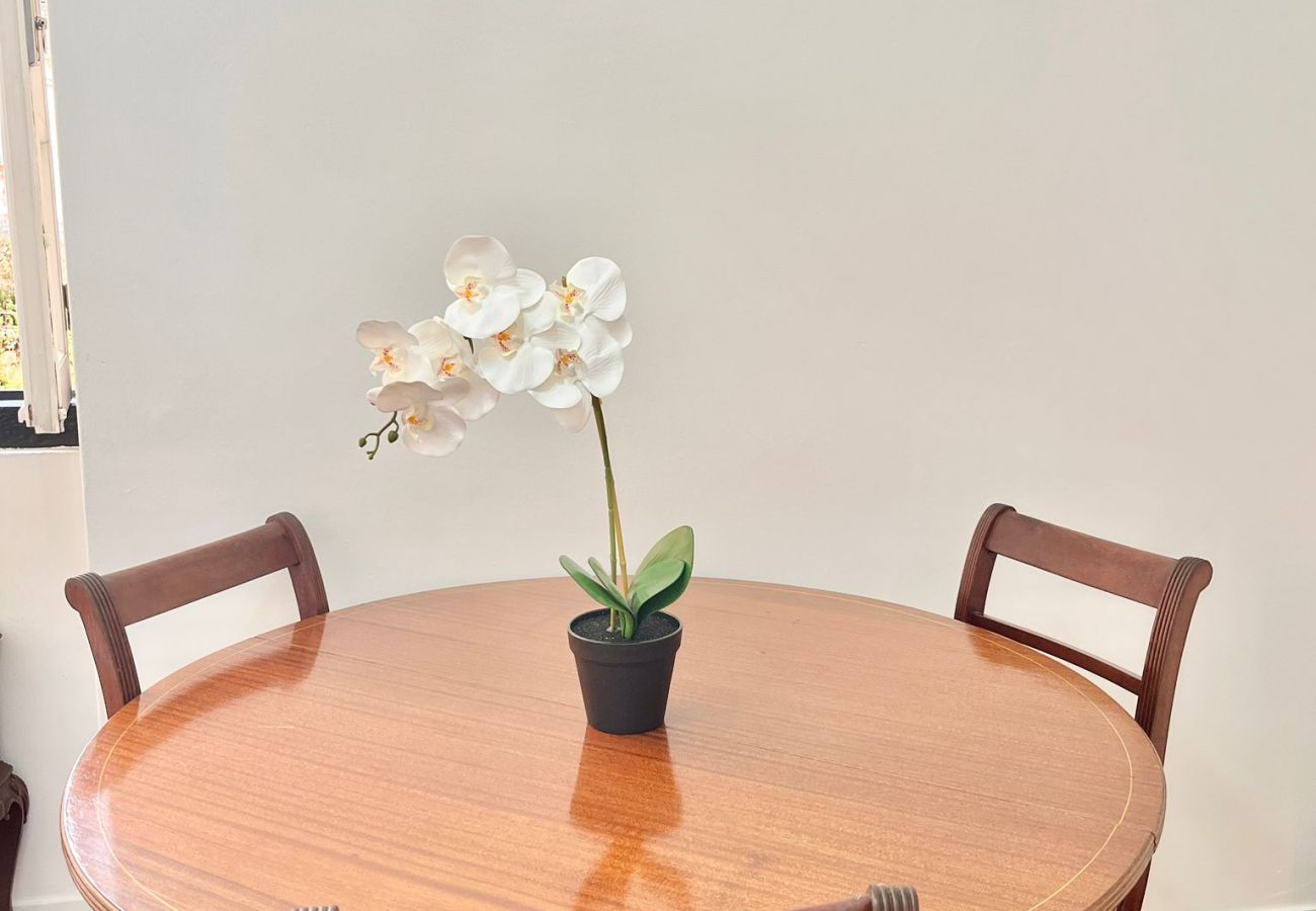 Dining room with a round wooden table, four chairs, and simple decor with a flower vase.