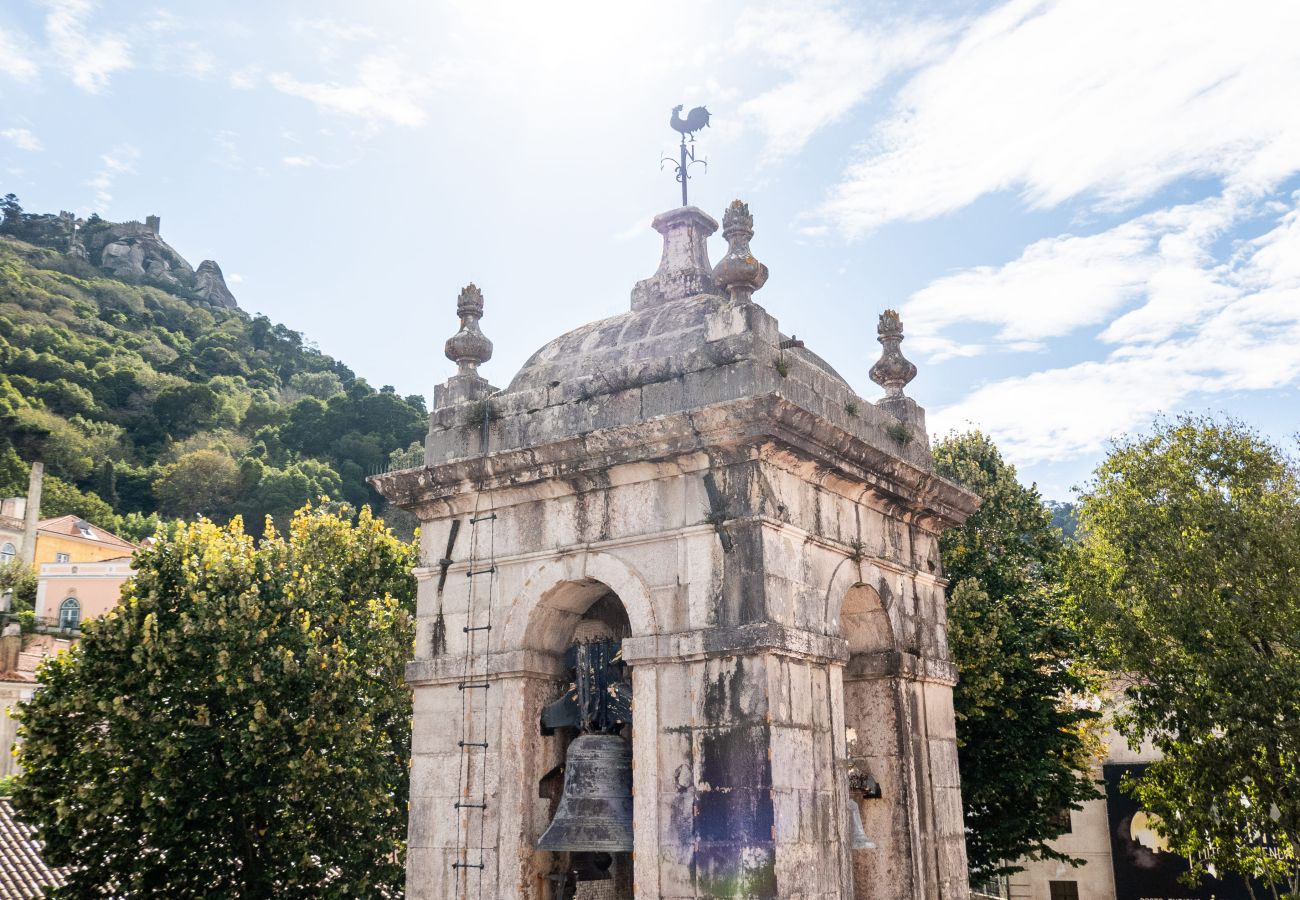 Sintra street with colorful buildings, a church tower, and tourists strolling.