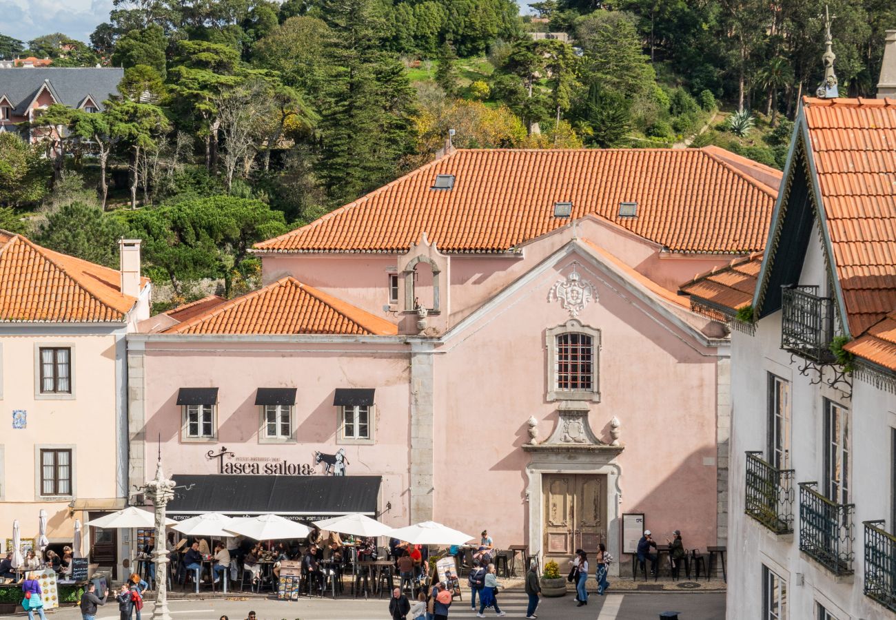 Aerial view of a busy street in Sintra, featuring outdoor cafés, umbrellas, and tourists exploring shops and restaurants.