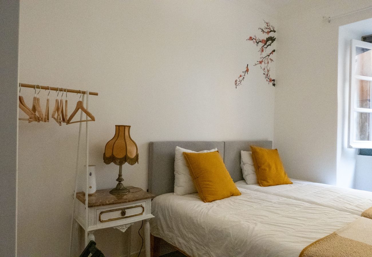  Bedroom with two single beds, white bedding with yellow accents, bedside table, and open clothes rack.