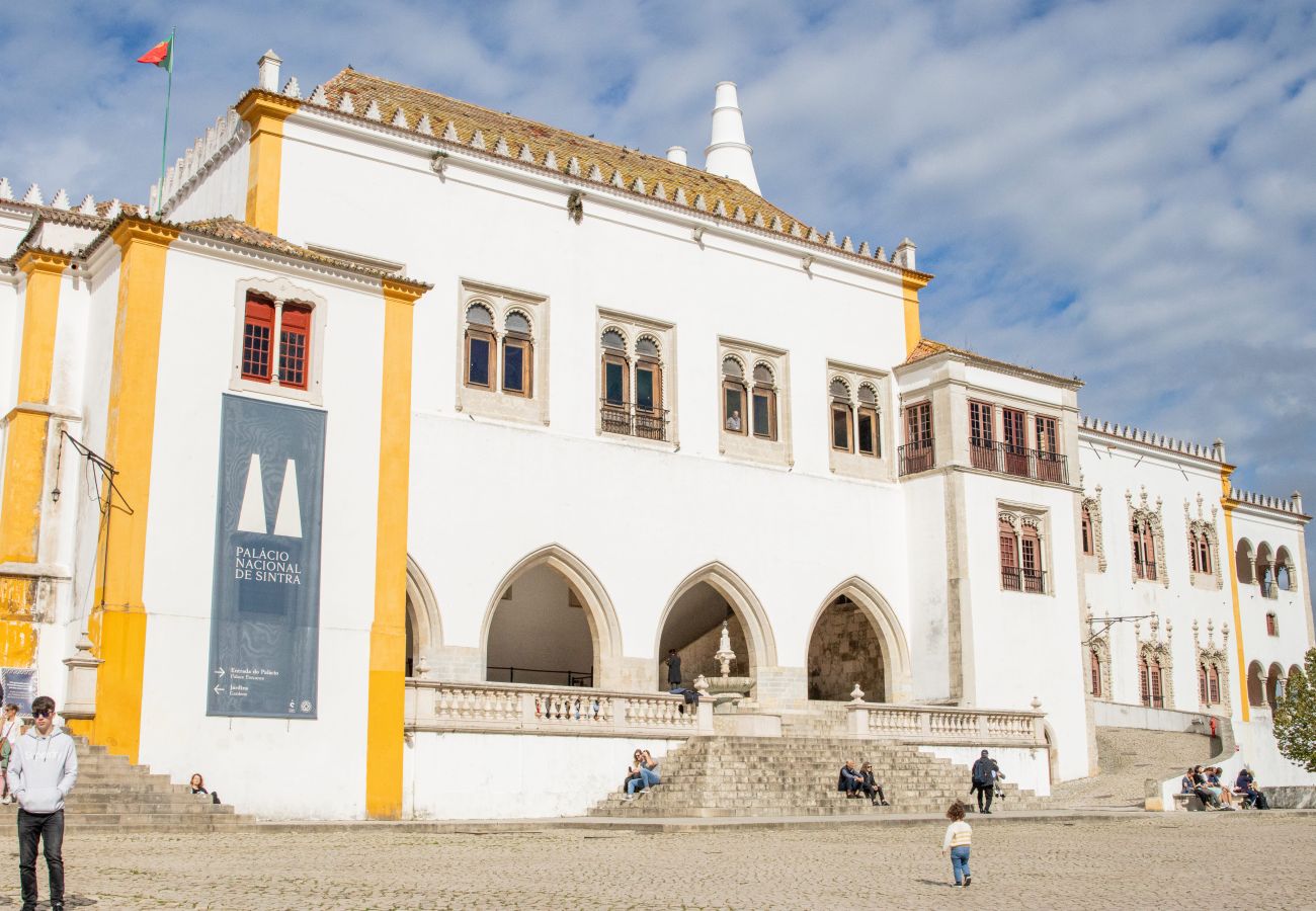 Facade of the National Palace of Sintra, featuring its iconic white chimneys and medieval architecture, under a blue sky.